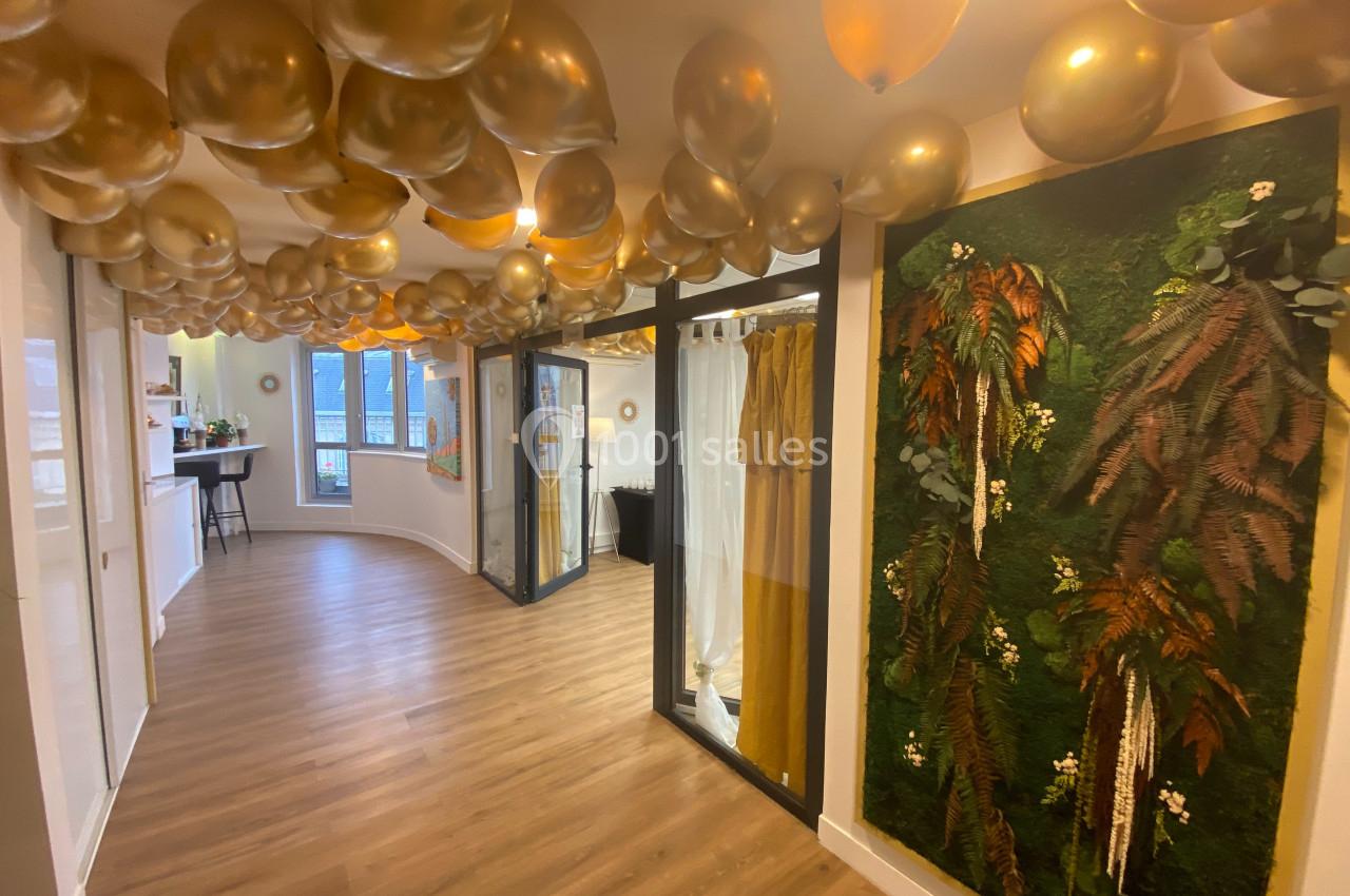 Plafond décoré de ballons dorés, mur végétal et sol en bois dans un espace lumineux avec baies vitrées.