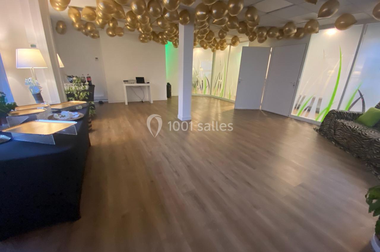 Salle lumineuse avec parquet, décorée de ballons dorés au plafond, tables dressées et plantes en arrière-plan.