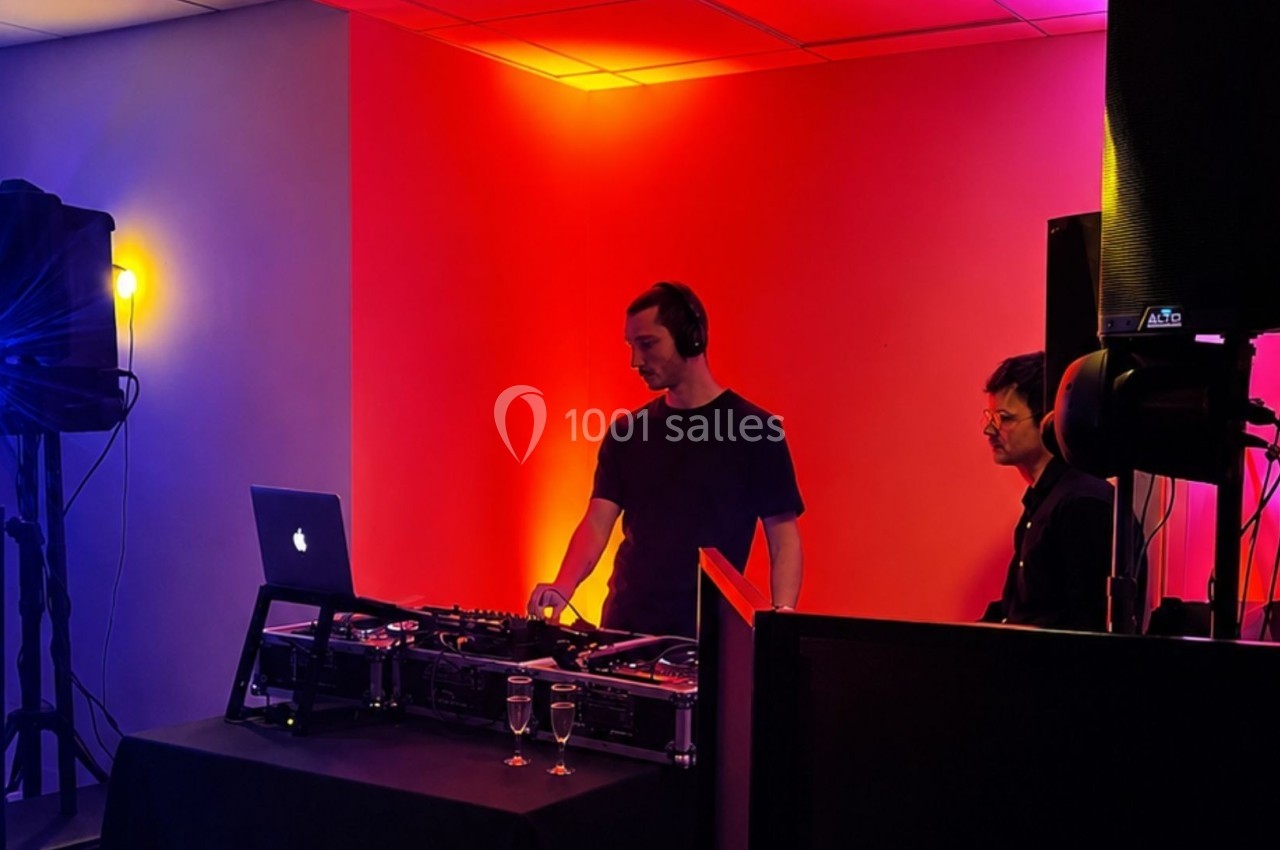 Un DJ mixe de la musique sur une table de mixage dans une salle éclairée par des lumières colorées.