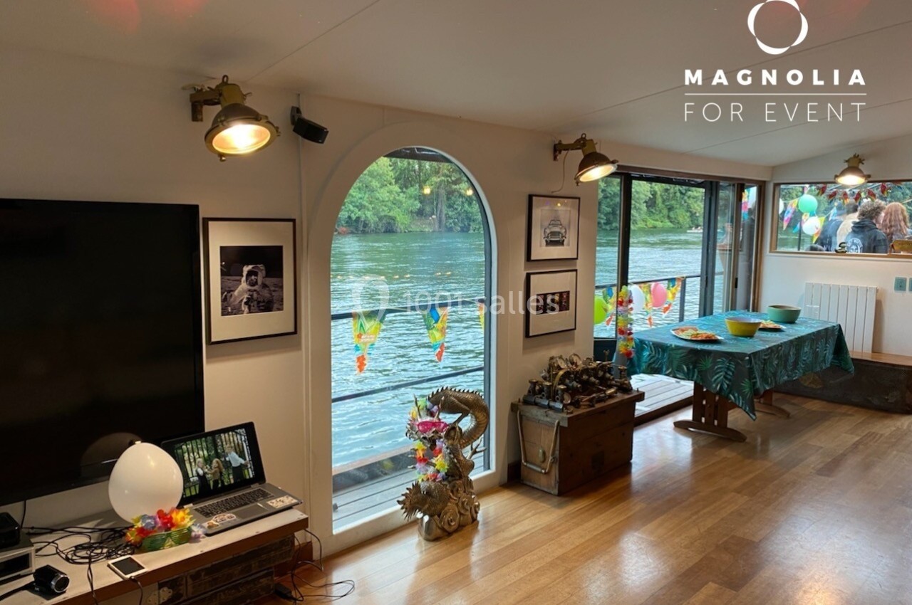 Salle décorée avec vue sur une rivière, table festive dressée et équipements multimédias à gauche.