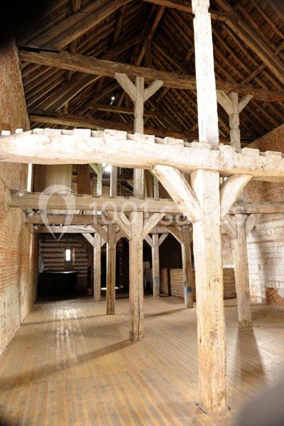 Intérieur d'une grange en bois avec des poutres apparentes, un sol en planches et des murs en briques.