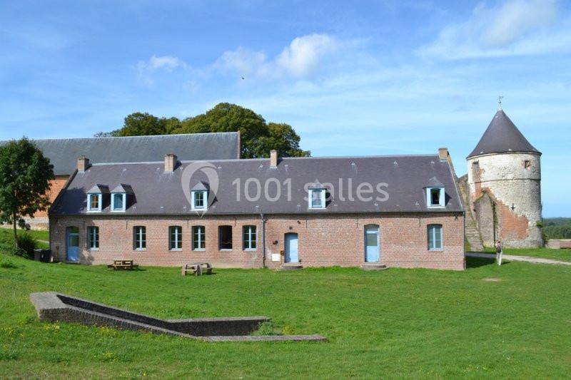 Bâtiment en briques rouges avec fenêtres bleues, une tour en pierre et un espace vert au premier plan.