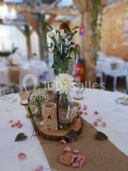 Centre de table rustique avec fleurs blanches, rondin de bois, bougies et pétales de rose sur une nappe beige.