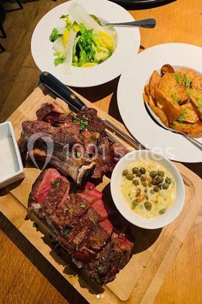 Planche de côte de bœuf grillée avec sauce, accompagnée de pommes de terre et salade verte.