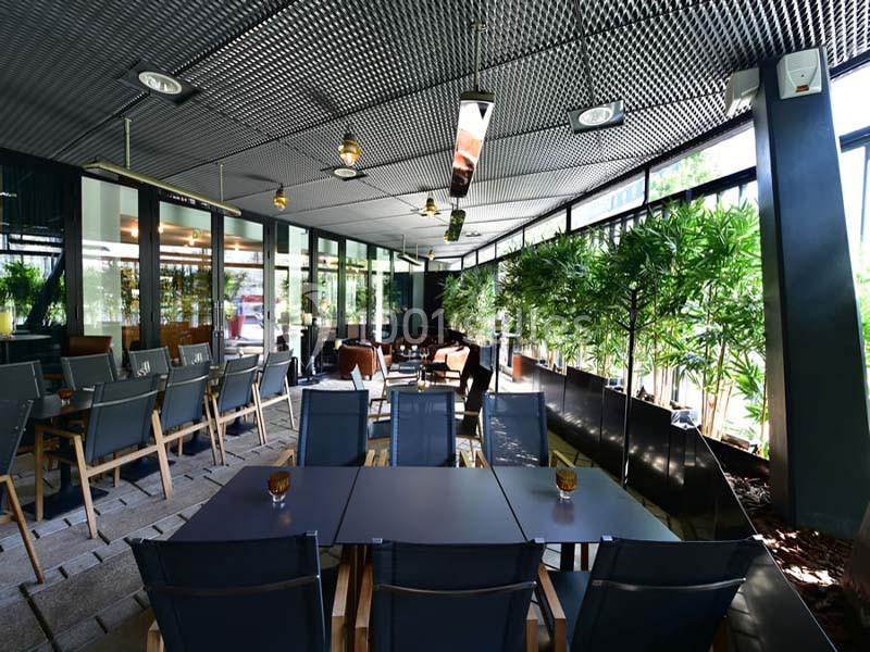 Terrasse couverte avec tables, chaises modernes et plantes en pot, éclairée par des suspensions et la lumière naturelle.