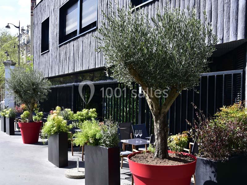 Arbres et plantes en pots décorent une terrasse extérieure devant un bâtiment moderne en bois.