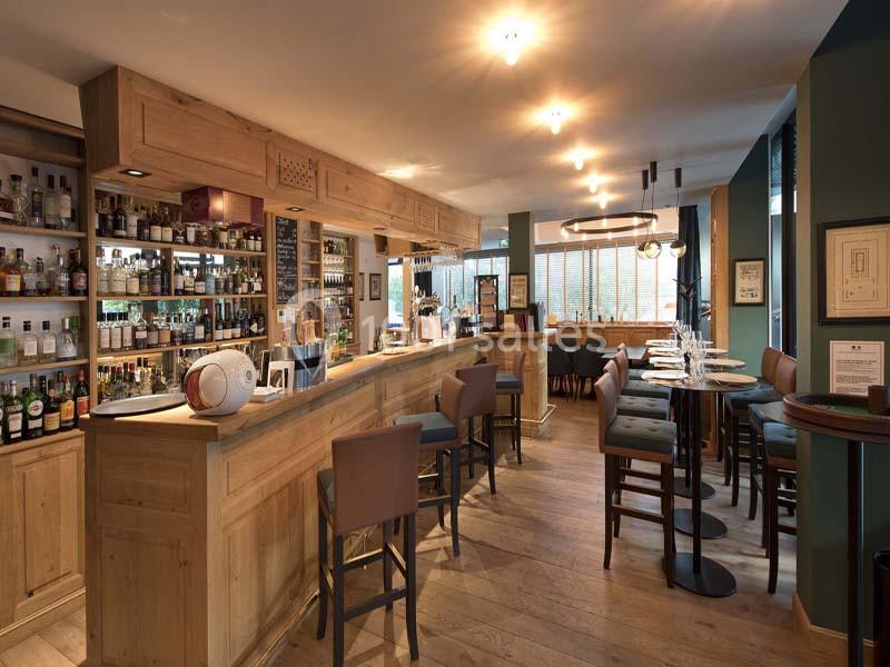 Intérieur d'un bar-restaurant avec comptoir en bois, étagères de bouteilles et tables dressées dans une ambiance chaleureuse.