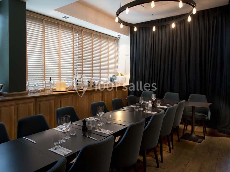 Salle de restaurant moderne avec une grande table dressée, des chaises bleues et un éclairage tamisé.
