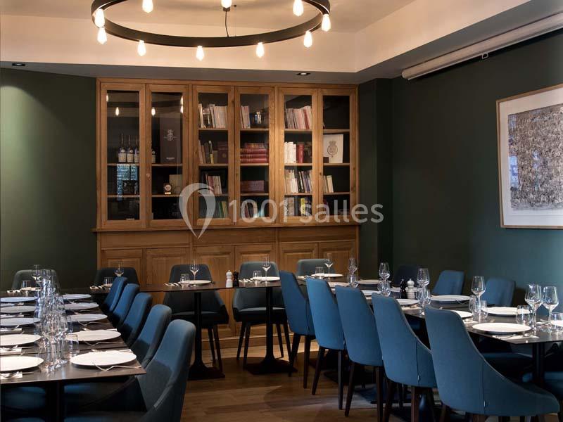 Salle de restaurant élégante avec tables dressées, chaises bleues et bibliothèque en bois en arrière-plan.