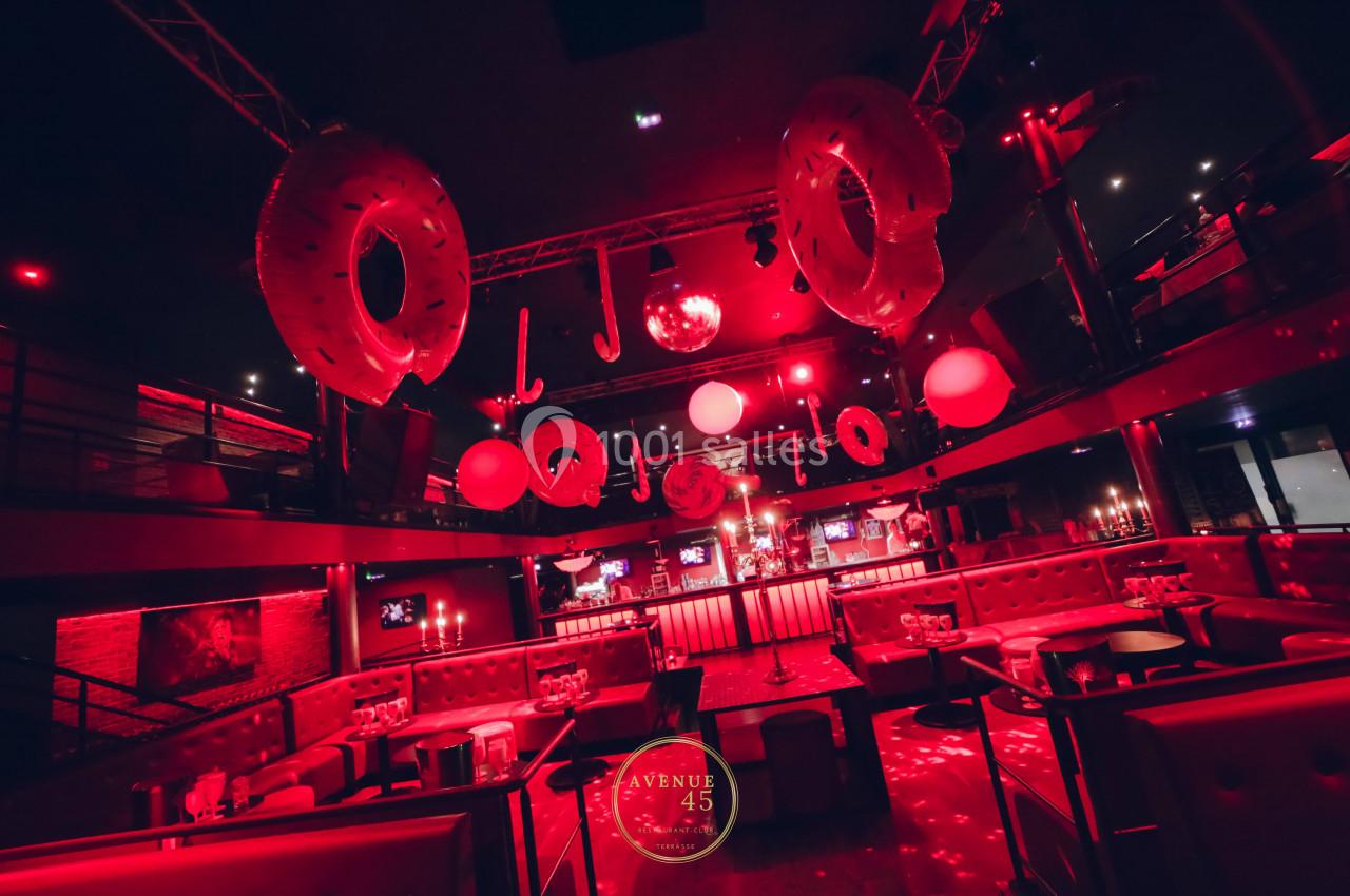 Salle de fête éclairée en rouge avec des décorations suspendues et des banquettes entourant une piste de danse.