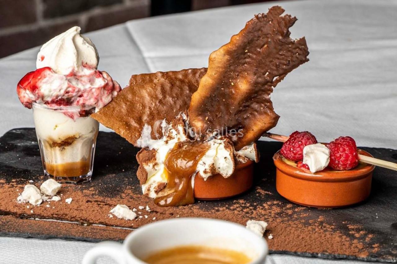 Dessert composé de crème glacée, framboises, chocolat, meringue et caramel, présenté sur une ardoise avec un café.