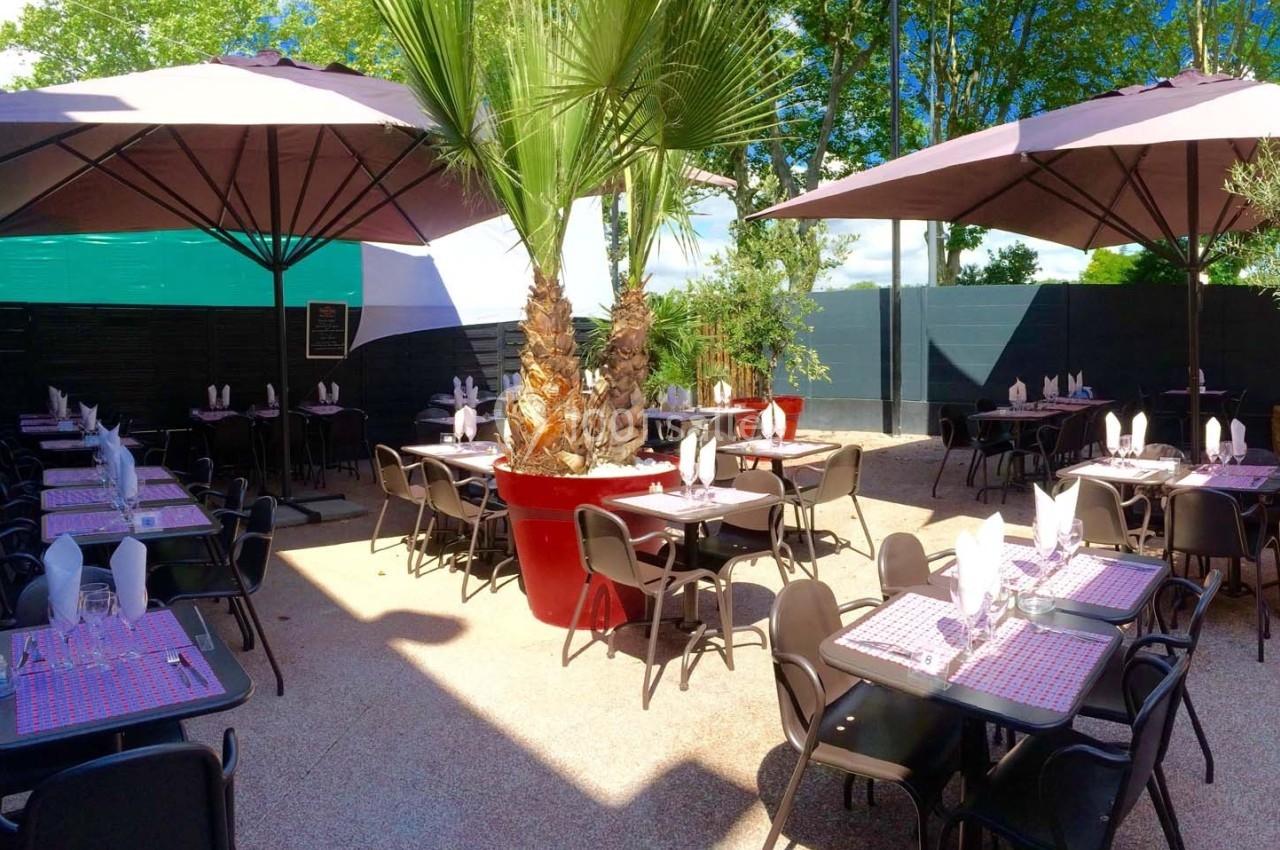 Terrasse de restaurant avec tables dressées, parasols et végétation, sous un ciel dégagé.