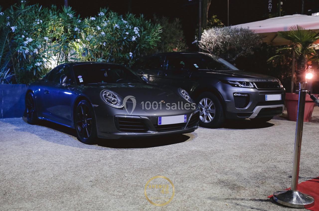Deux voitures stationnées de nuit, une Porsche grise et un SUV Range Rover, entourées de végétation et d'éclairage urbain.