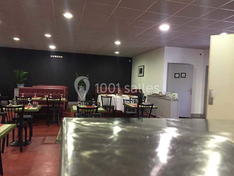 Salle de restaurant avec tables dressées, chaises noires, banquettes rouges et plantes décoratives sur fond sombre.