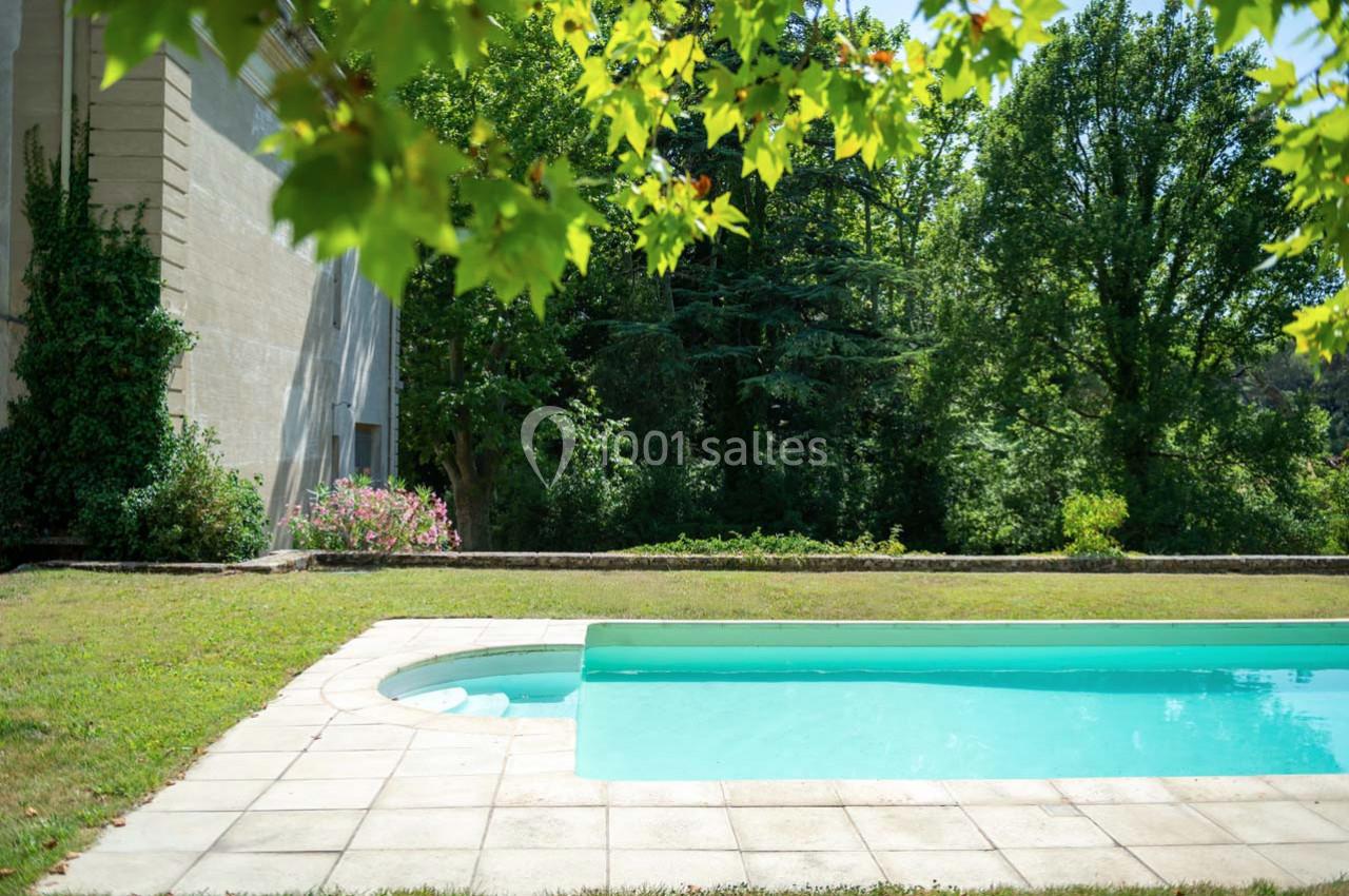 Piscine extérieure entourée de pelouse, bordée d'arbres et d'un mur en pierre dans un cadre verdoyant.