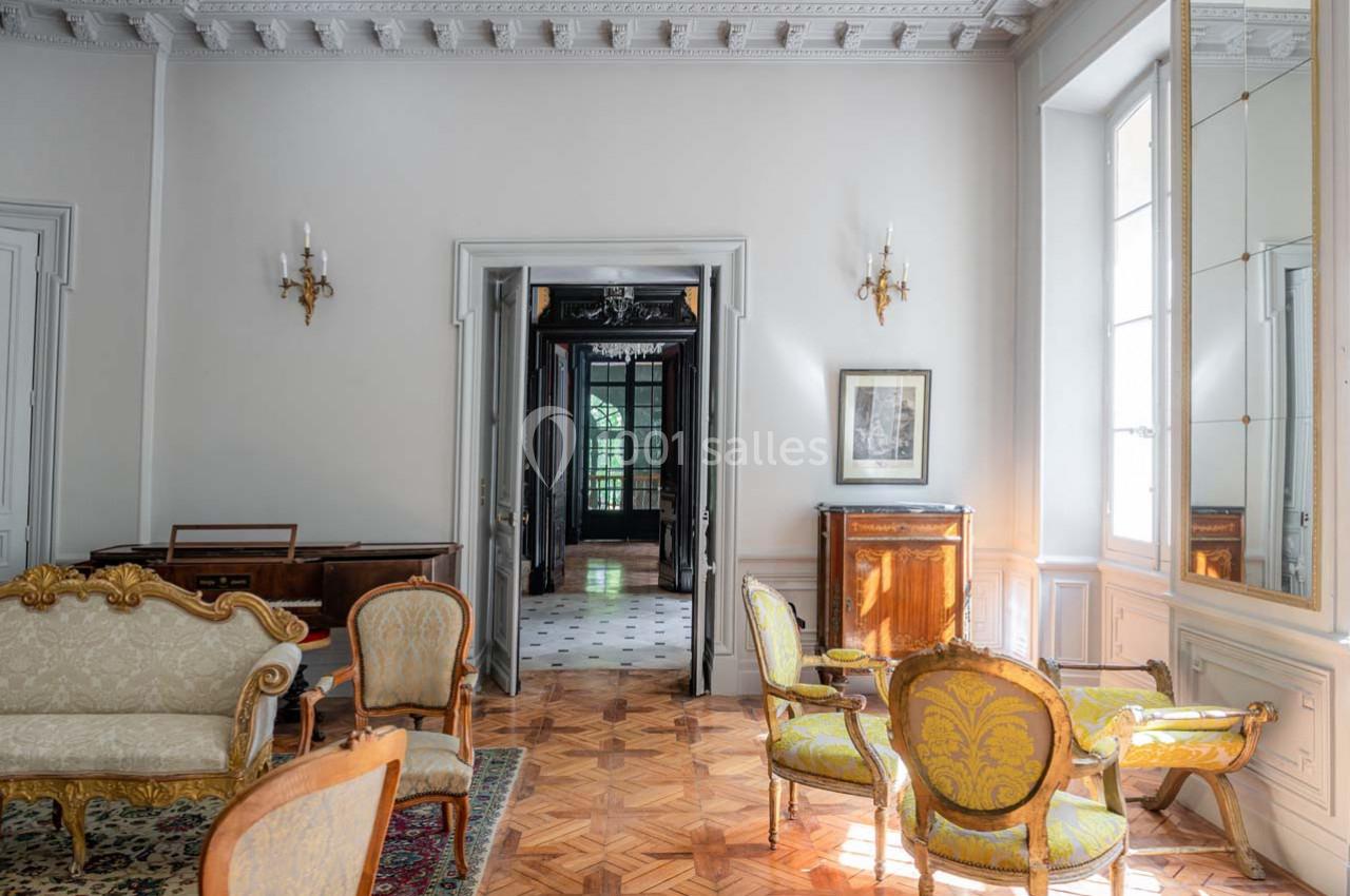 Salon élégant avec parquet en bois, mobilier classique, moulures au plafond et vue sur un couloir lumineux.