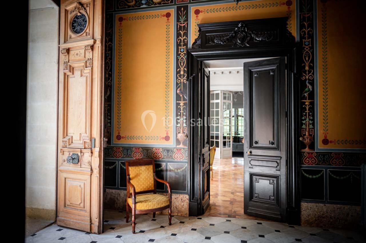 Intérieur d'une pièce élégante avec murs ornés, porte en bois sculpté, fauteuil ancien et sol en marbre.