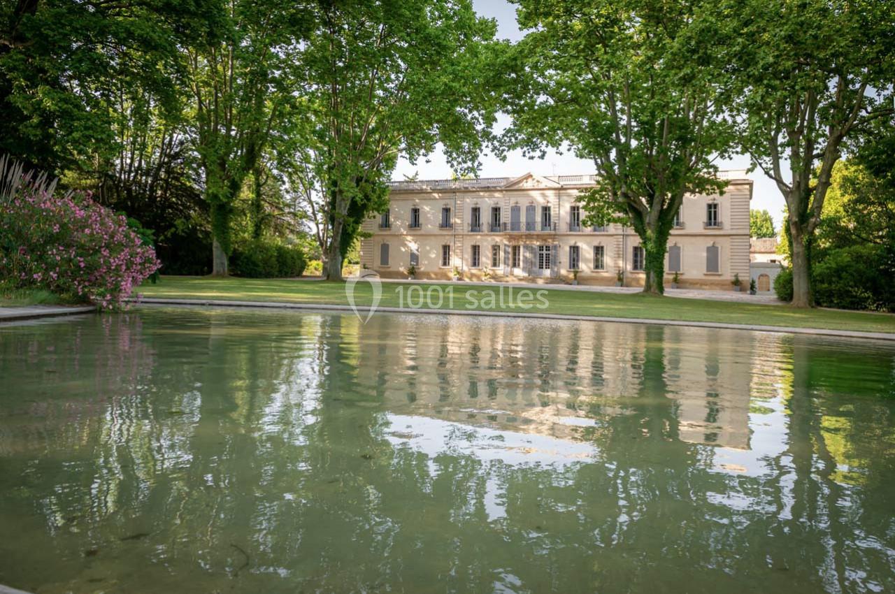 Façade d'un grand bâtiment entouré d'arbres, reflétée dans un bassin au premier plan.