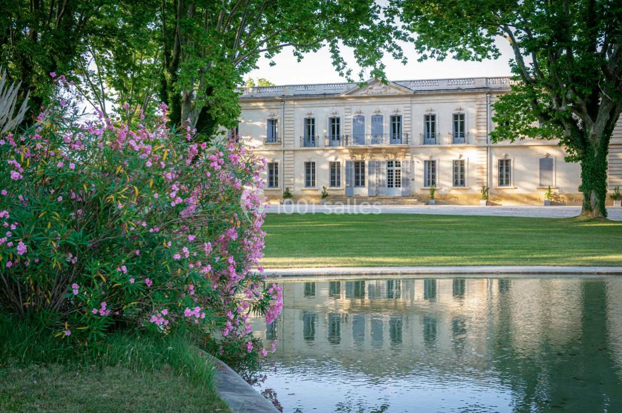 Façade d'un bâtiment classique entouré d'arbres, avec un étang reflétant l'ensemble au premier plan.