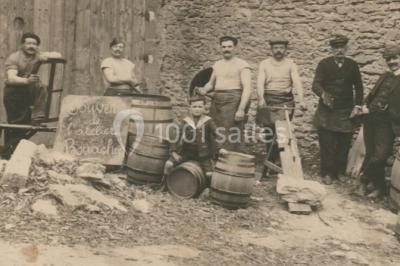 Une voiture bleue traverse un chemin bordé de vignes et de murets en pierre sous un ciel dégagé.