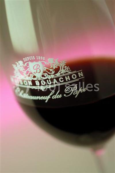 Verre de vin rouge avec le logo ’Maison Bouachon Châteauneuf-du-Pape’ gravé, éclairé par une lumière rose.