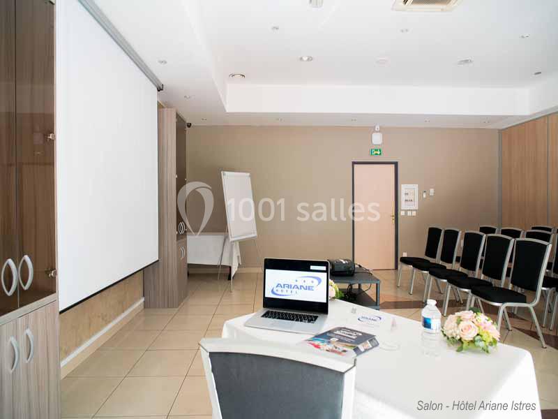Salle de réunion lumineuse avec écran de projection, chaises alignées, table équipée d'un ordinateur portable et documents.