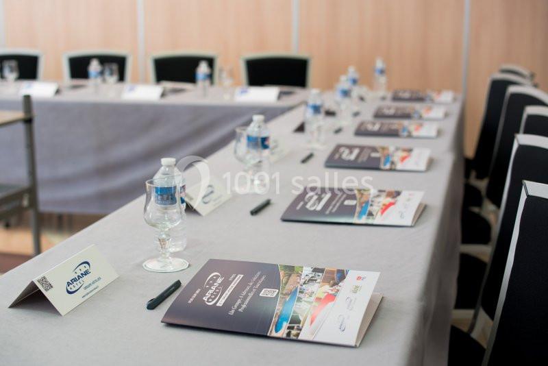Salle de réunion avec une table dressée, contenant des brochures, des bouteilles d'eau et des verres alignés.