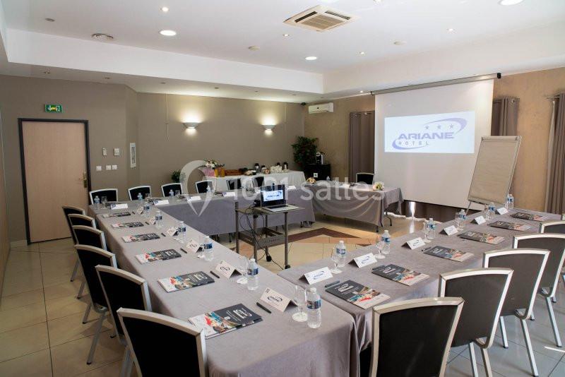 Salle de réunion équipée avec tables disposées en U, écran de projection, paperboard et matériel de conférence.