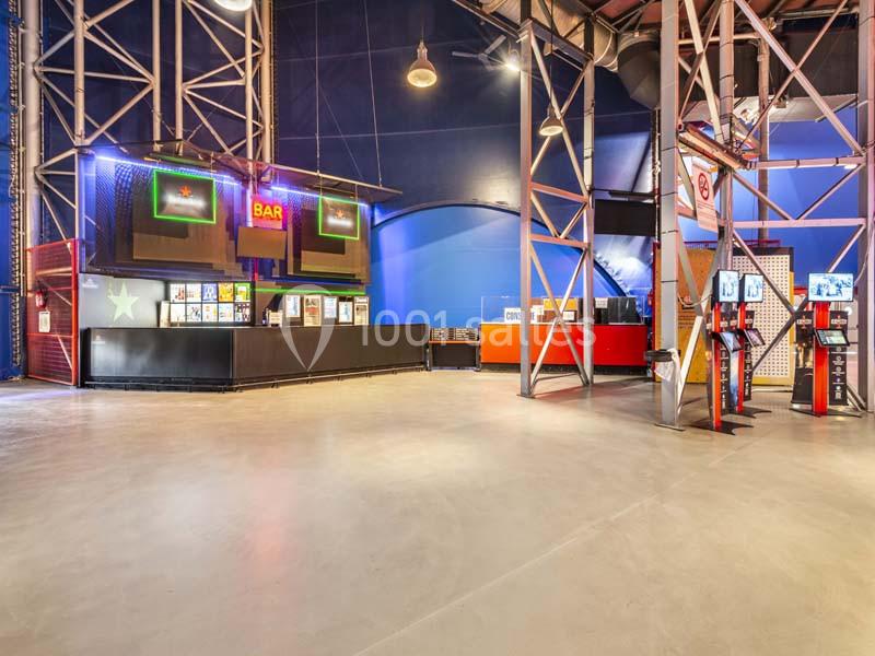 Espace intérieur avec un comptoir de bar éclairé, des bornes interactives et une structure métallique apparente.