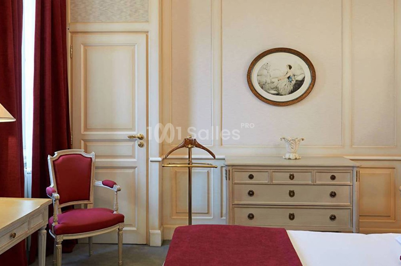 Chambre élégante avec mobilier classique, rideaux rouges, lampe sur une table et tableau rond au mur.