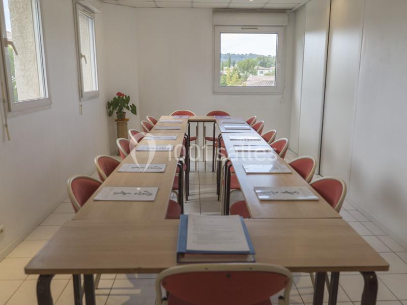 Salle de réunion lumineuse avec une grande table rectangulaire, des chaises rouges et des documents disposés.