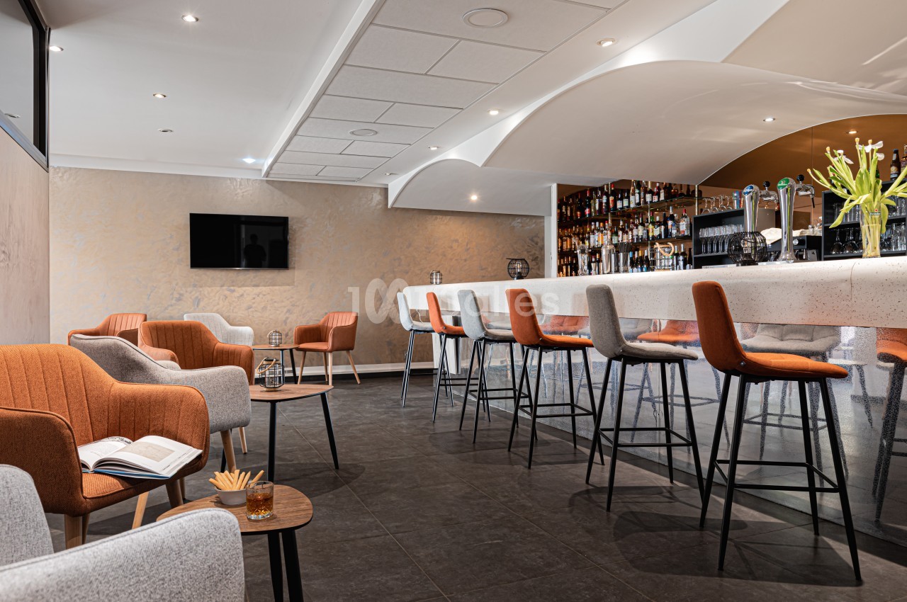 Espace lounge moderne avec bar, chaises hautes, fauteuils confortables et éclairage tamisé.