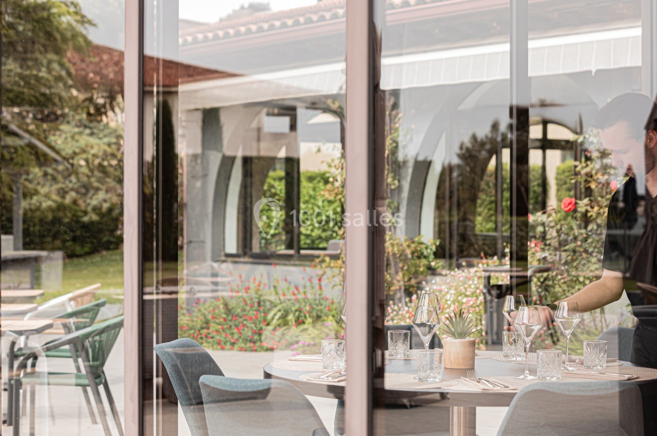 Un serveur prépare une table élégamment dressée dans un restaurant avec vue sur un jardin fleuri.
