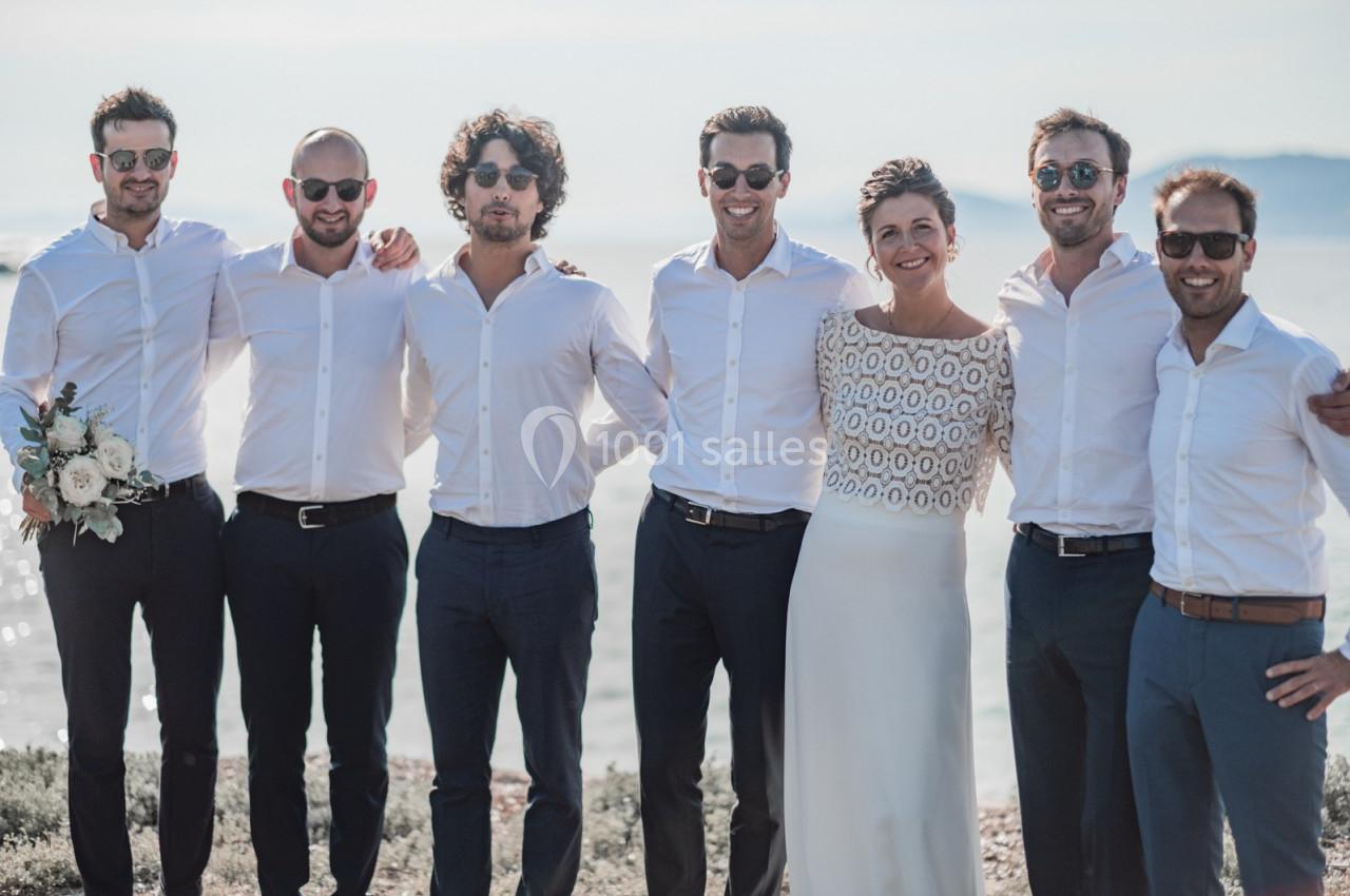 Un groupe de personnes en tenue élégante, souriant devant un paysage côtier ensoleillé.