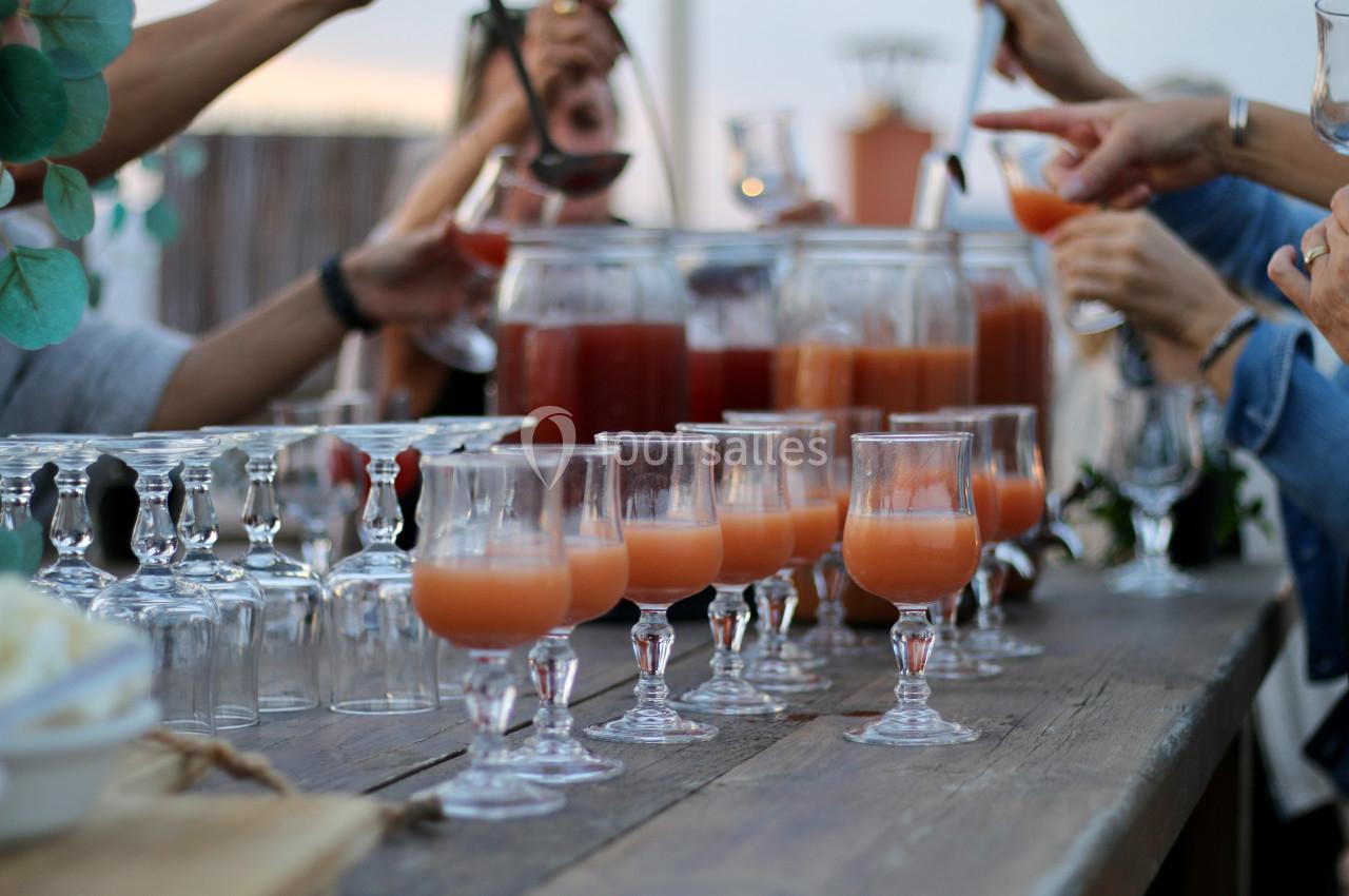 Des verres de cocktail orange disposés sur une table en bois, entourés de mains servant des boissons.