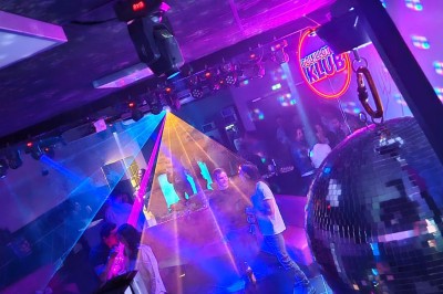 Miniature Location salle Hyères (Var) - La Réserve Hyères - Giens #34 Des personnes dansent en couple sur une piste éclairée par des lumières colorées, tandis que d'autres sont assises autour.