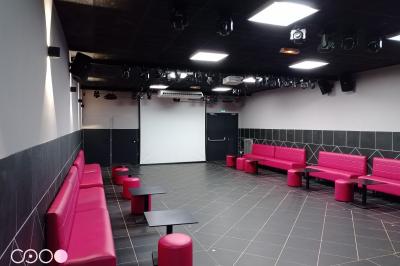 Miniature Le Club Des personnes dansent en couple sur une piste éclairée par des lumières colorées, tandis que d'autres sont assises autour.