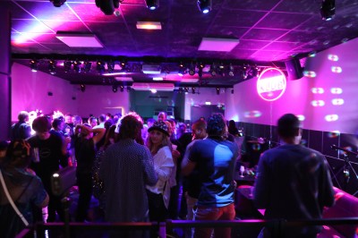 Miniature Le Club soirée Nouvel An Des personnes dansent en couple sur une piste éclairée par des lumières colorées, tandis que d'autres sont assises autour.