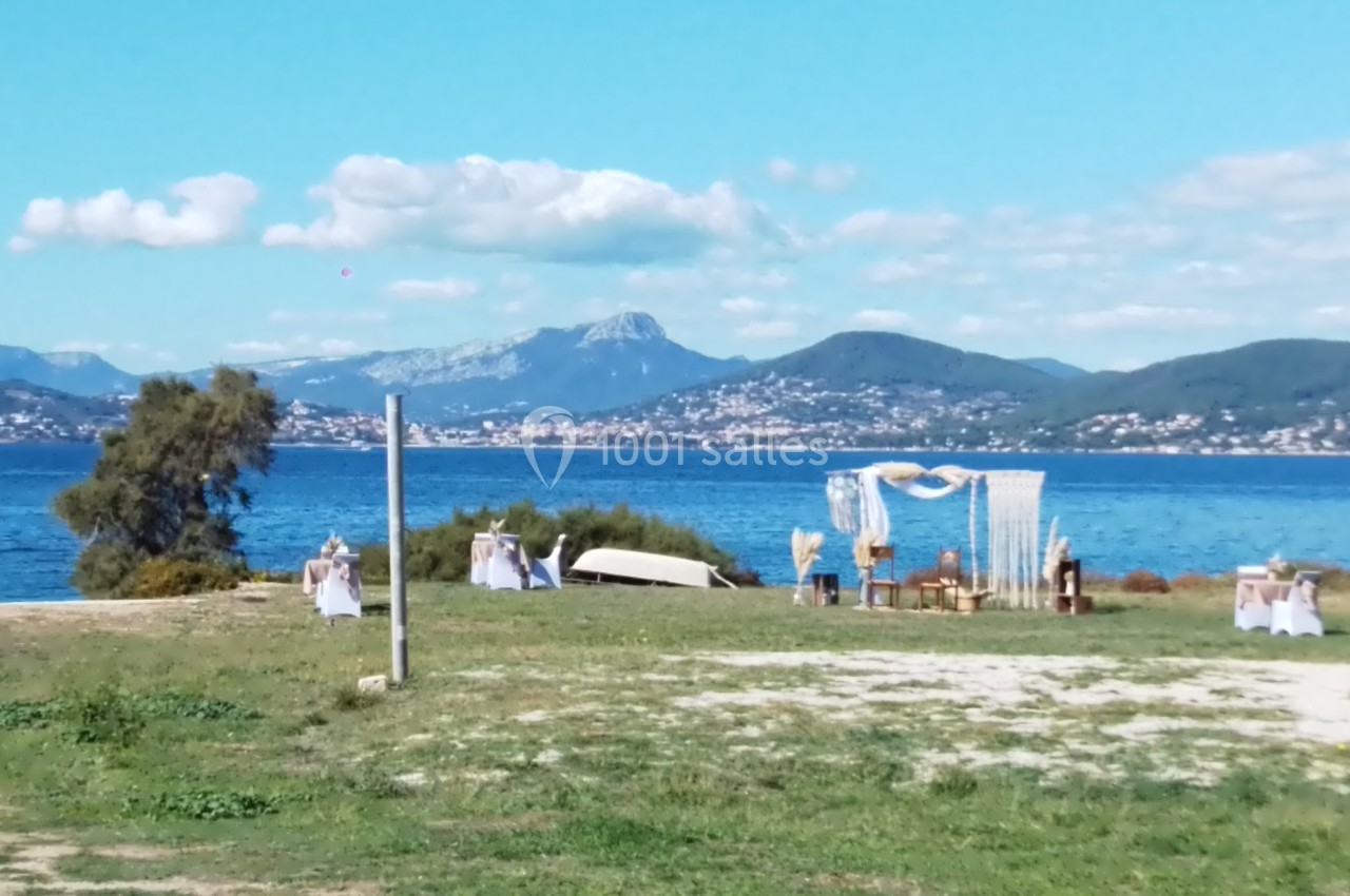 Cérémonie en plein air près d'un lac, avec une arche décorée et des montagnes en arrière-plan.