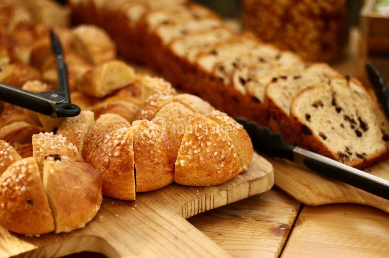 Location salle Hyères (Var) - La Réserve Hyères - Giens #4 Assortiment de pains tranchés et viennoiseries disposés sur des planches en bois avec des pinces de service.