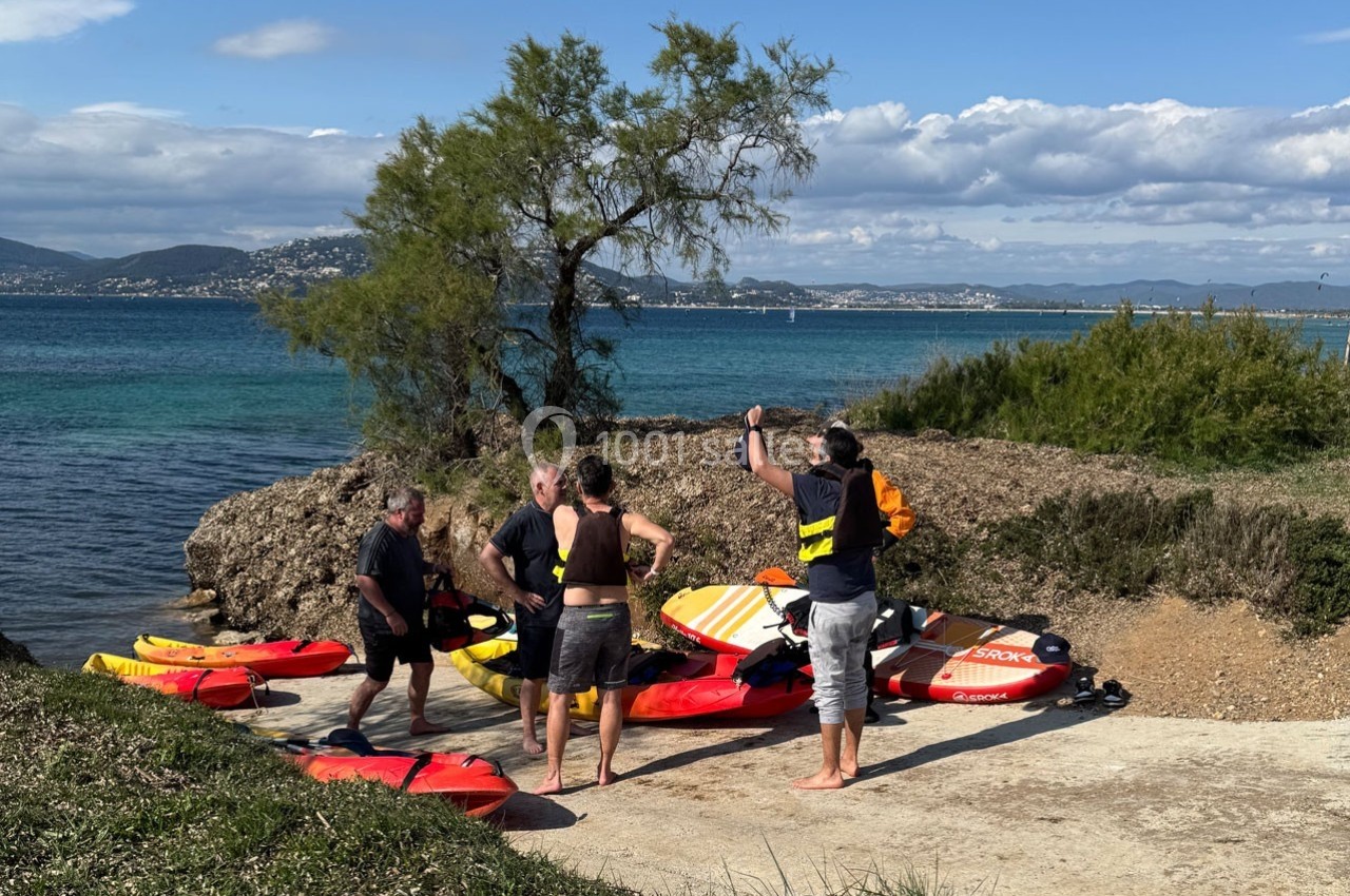 Location salle Hyères (Var) - La Réserve Hyères - Giens #3 Un groupe de personnes prépare des planches de paddle sur une rampe près d'une étendue d'eau bordée de végétation.