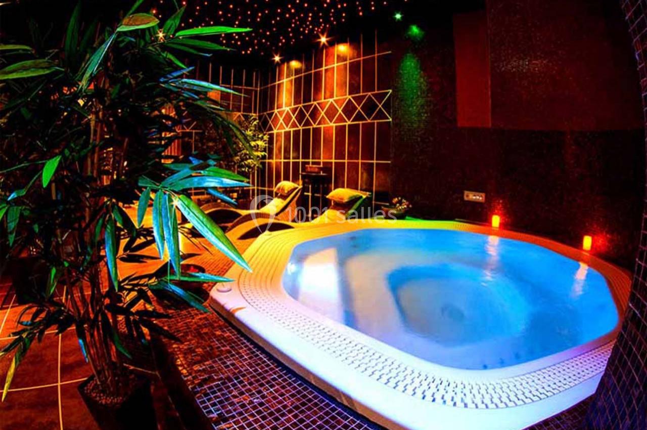 Aphrodite SPA Bain à remous éclairé par des lumières colorées, entouré de plantes et de chaises longues dans une ambiance tamisée.
