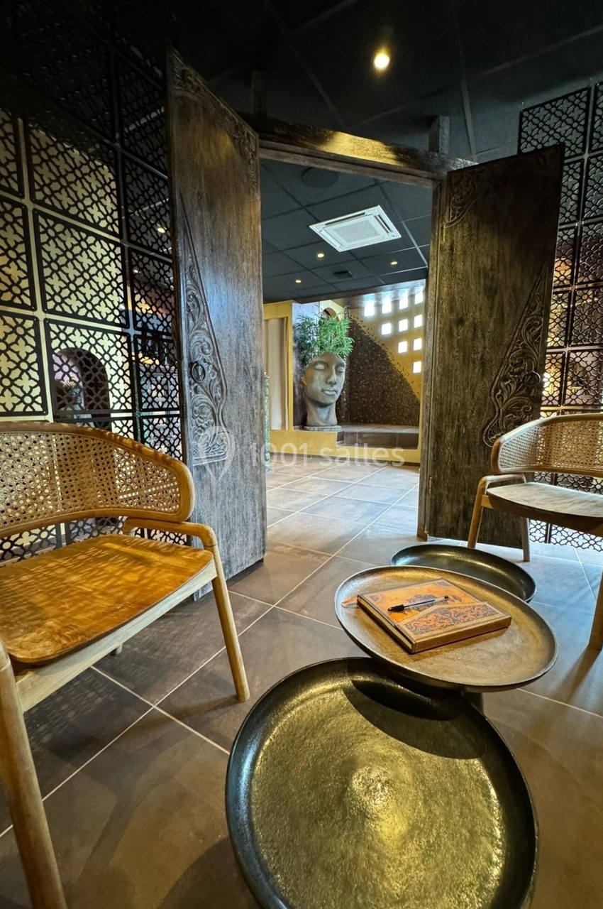 Aphrodite SPA Deux fauteuils en rotin entourent une table basse avec un livre, dans un espace décoré de motifs asiatiques et une statue…