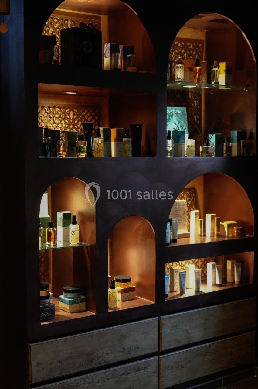 Aphrodite SPA Étagères éclairées contenant des flacons de parfum et des produits cosmétiques dans un décor sombre et élégant.