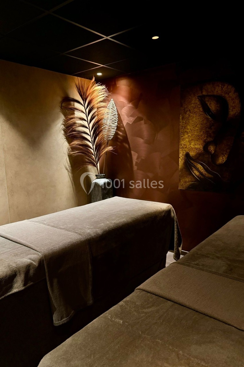 Aphrodite SPA Salle de massage tamisée avec deux tables recouvertes de draps bruns et une décoration murale apaisante.