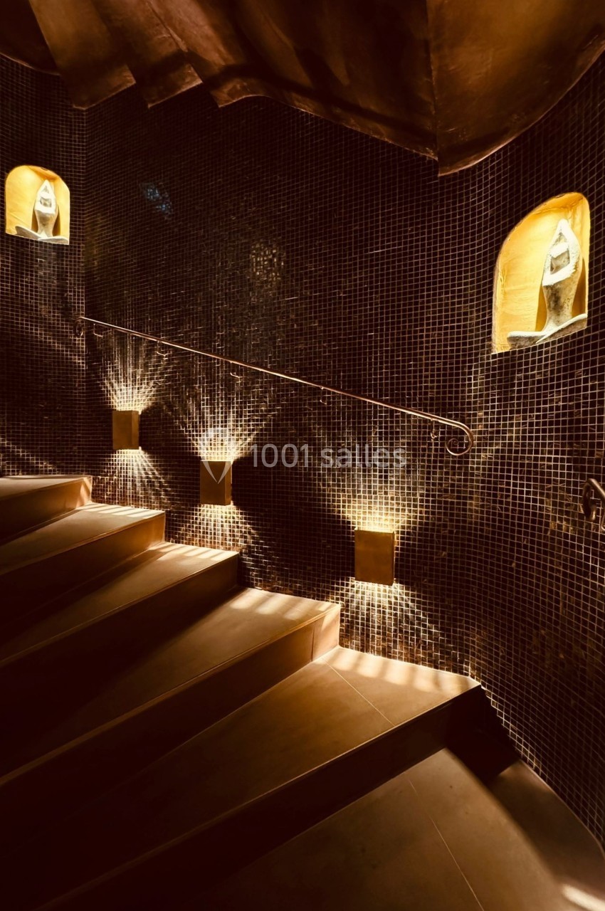Aphrodite SPA Escalier en colimaçon avec des murs recouverts de mosaïques sombres, éclairé par des niches lumineuses.