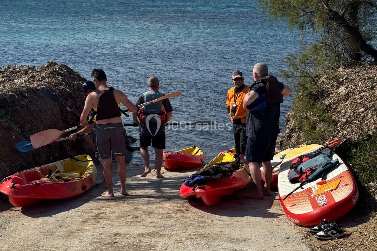 Cohésion sur le Terrain Les Pieds dans l'Eau Des personnes préparent des kayaks sur une rampe en bord de mer, avec une vue sur des collines à l'horizon.