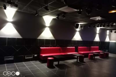 Miniature Le Club Salle de massage tamisée avec deux tables recouvertes de draps bruns et une décoration murale apaisante.