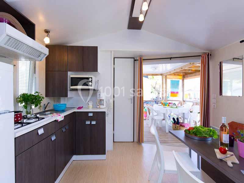 Mobil-home Cuisine moderne avec meubles en bois sombre, table dressée, et vue sur une terrasse lumineuse aménagée.