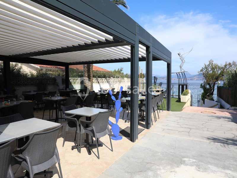 Restaurant Le Solarium bord de mer Terrasse couverte d'un restaurant avec des tables et chaises, vue sur la mer et sculpture moderne à proximité.